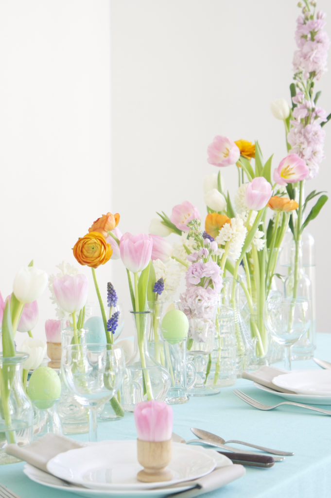 Gather all your glassware and add a fresh flowers and colored eggs in springtime hues to create a sweet and welcoming spring table.  I love the idea of using egg cups as tiny flower holders. easter decor - spring decorating ideas - spring table - easter table - easter centerpiece - table setting - tablescape