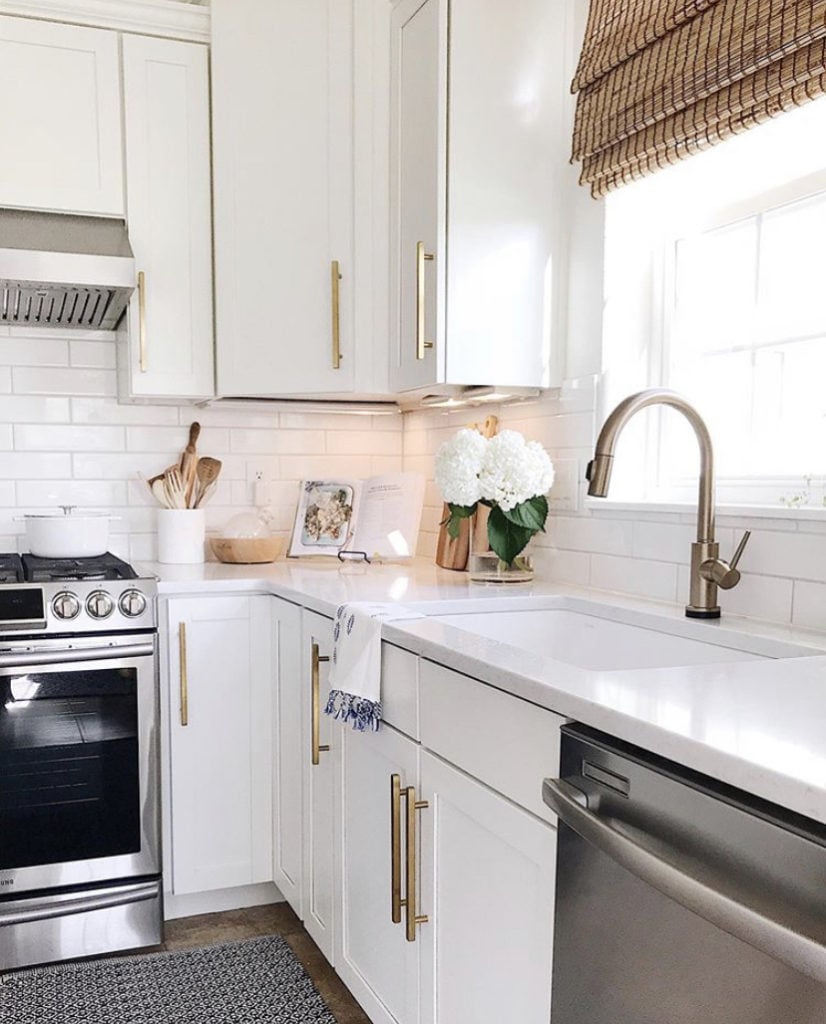 Modern coastal kitchen with white cabinets, gold faucet, brass cabinet pulls, a blue and white rug, and bamboo window shades - jane at home