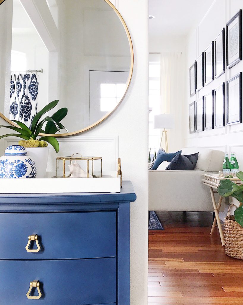 Blue cabinet with brass pulls, white tray and round gold mirror in entryway How to shop your home for a fresh new look - jane at home