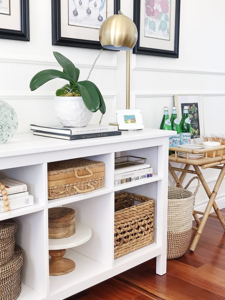 White shelf decor styled with baskets, plants, books and artwork, along with a bamboo bar cart