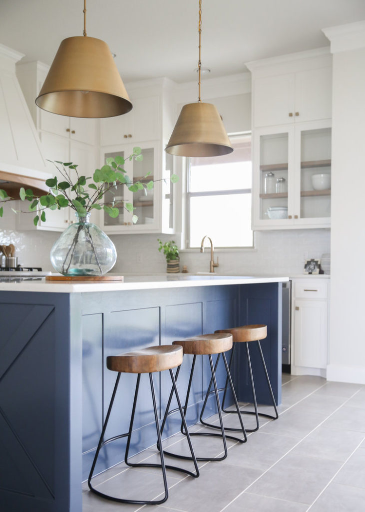 Beautiful kitchen design with blue island, white cabinets with glass front and side inserts, and brass conical pendants by House Sprucing