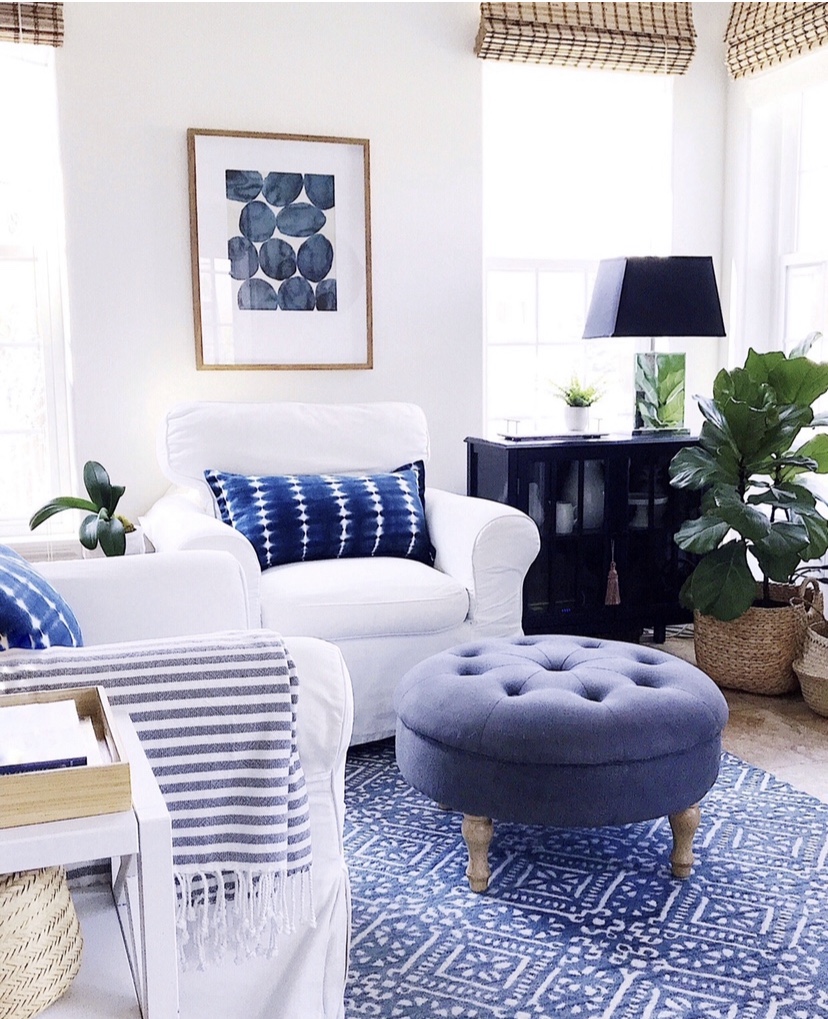 Summer home decor essentials in the living room - artwork, stripes, blue and white indigo shibori pillows, baskets, round ottoman and slipcovered chairs - jane at home