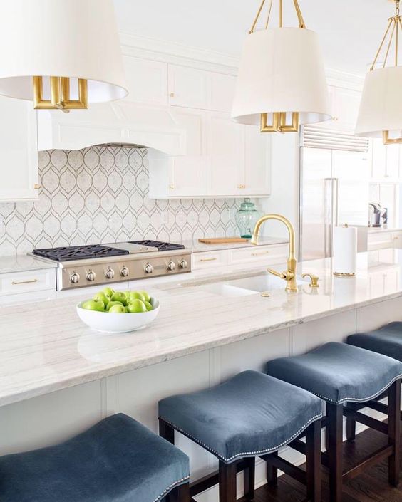 Beautiful kitchen with unique backsplash, white and gold pendant lights, and blue counter stools