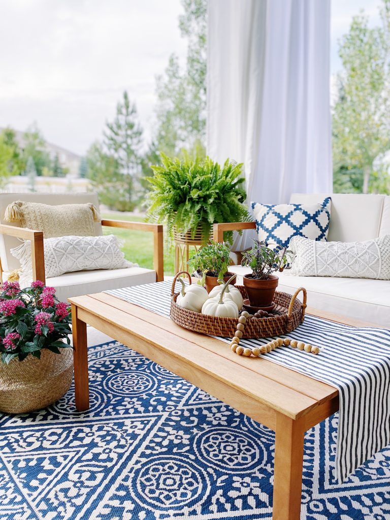 Our backyard patio design with a blue and white rug, white outdoor curtains, and wood furniture - jane at home - outdoor ideas - covered porch - covered patio - outside ideas - concrete patio decorating ideas 