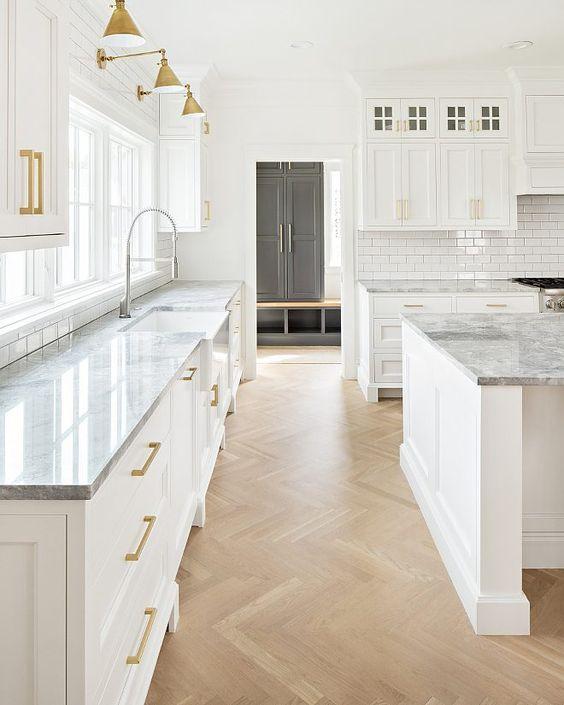 Love this beautiful kitchen design with wood herringbone floors, marble countertops, white kitchen cabinets, and brass hardware and sconces - the Fox Group
