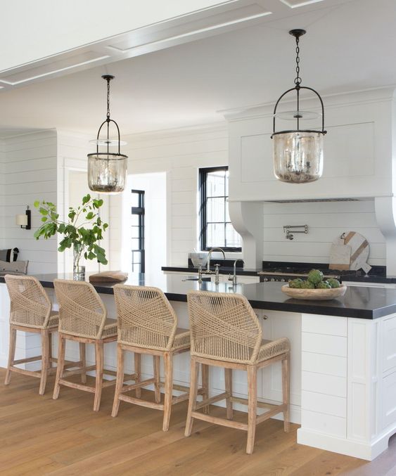 Beautiful white farmhouse kitchen with black countertops and woven stools - 2 hawks designs