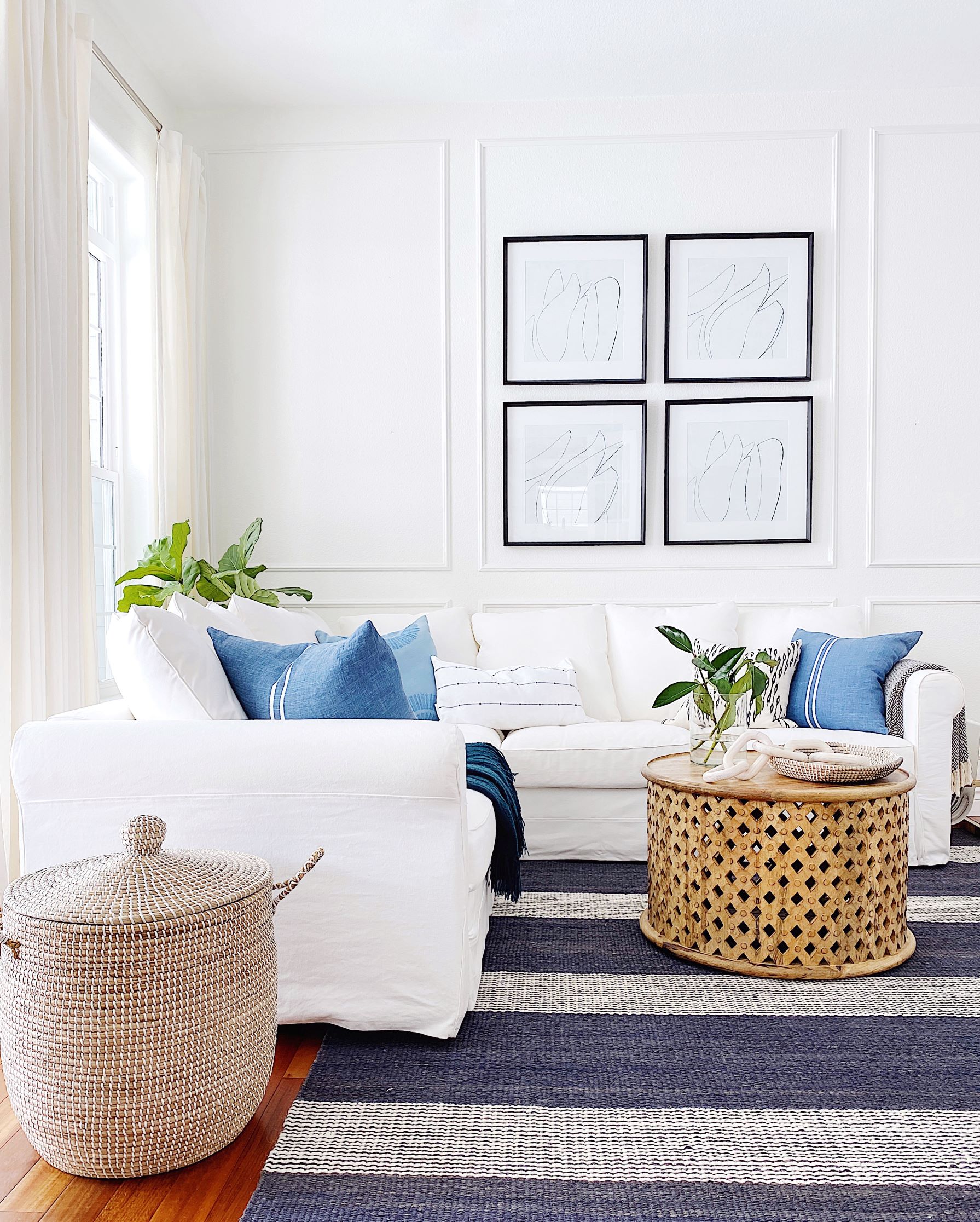 Blue and white in the living room with a jute rug, black framed artwork and panel molding trim on the walls - jane at home #livingroom #livingroomdecor #coastaldecor #coastalstyle #livingroomideas