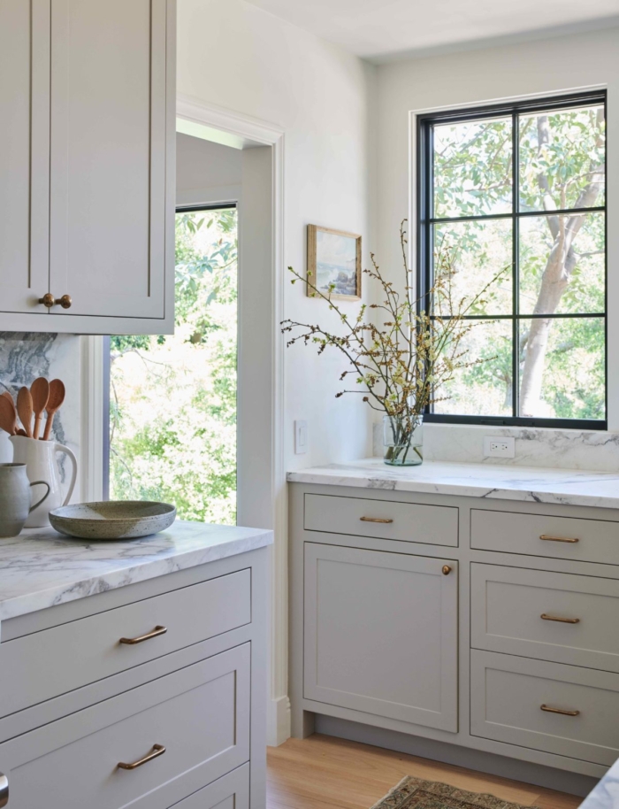 This beautiful gray and white kitchen, with its brass accents, marble countertops, and black framed windows, is a beautiful blend of traditional and modern design. From Amber Interior Design | Photo By Tessa Neustadt