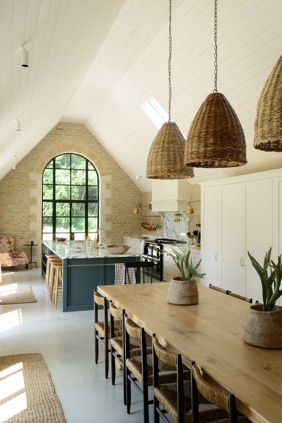 Love this beautiful European style kitchen design with a stone wall, vaulted ceiling, large window, and woven pendant lighting - devol kitchens