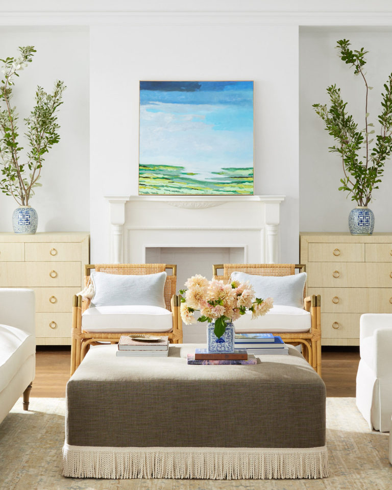 Love this beautiful living room with a fringed ottoman, woven side chairs and coastal artwork