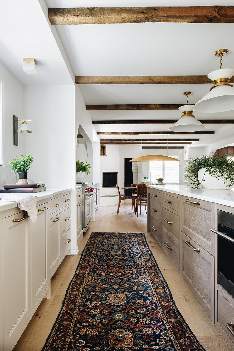 Beautiful spaces of the week: warm and wonderful kitchen design with wood beams, rich Turkish Oushak runner, light wood island, and unique white and brass pendant lights - Jean Stoffer Design #kitchendesign #kitchendecor #kitchenideas