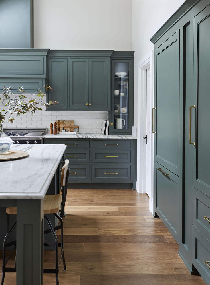 Love this beautiful kitchen design with dark green kitchen cabinets, brass hardware, a white subway tile backsplash, and marble countertops - Sherwin Williams Pewter Green - Emily Henderson
