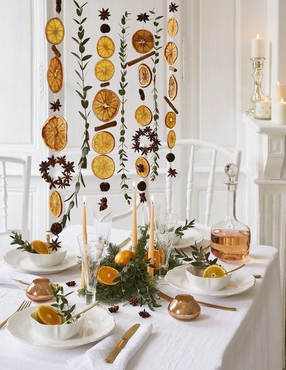 A gorgeously styled Christmas dinner table with orange and citrus slices, cinnamon sticks and greenery creating a striking hanging decoration over the table