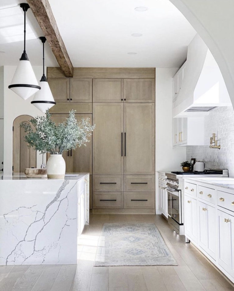 Love this modern kitchen design with marble waterfall countertops on the kitchen island, chic pendant light fixtures, and light wood beams and cabinets - kitchen island ideas - kitchen lighting - mixing metal finishes in the kitchen - vivir design