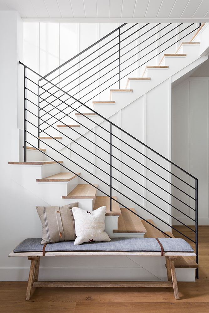 Such a fresh and beautiful staircase, with its white paneling, black iron railings, and light wood stair treads!  I love the rustic bench, too. stairway ideas - railings - black and white - entryway ideas - staircase