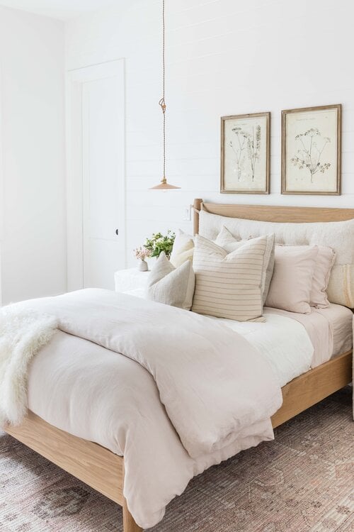 Lovely boho bedroom with layered bedding, floral artwork and neutral decor 