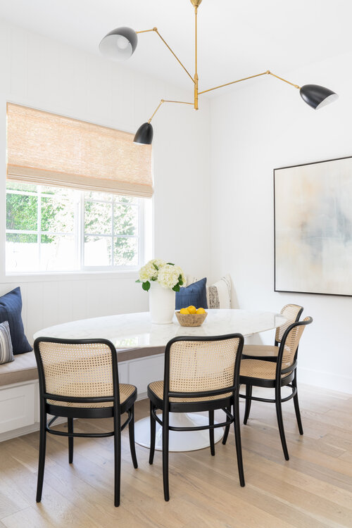 I love this modern breakfast nook with an oval tulip table, banquette seating, and modern black and cane dining chairs - Livingston Interiors