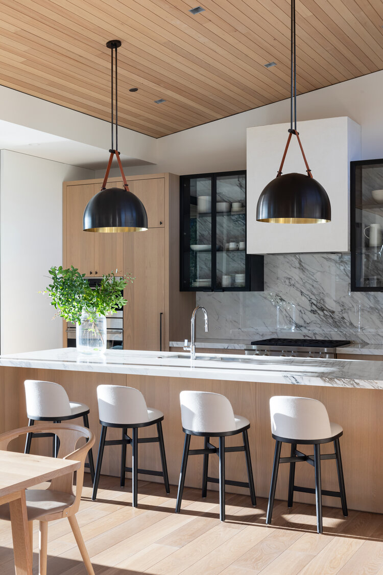Stunning organic modern kitchen design with black pendant lights, light wood cabinets and curved counter stools