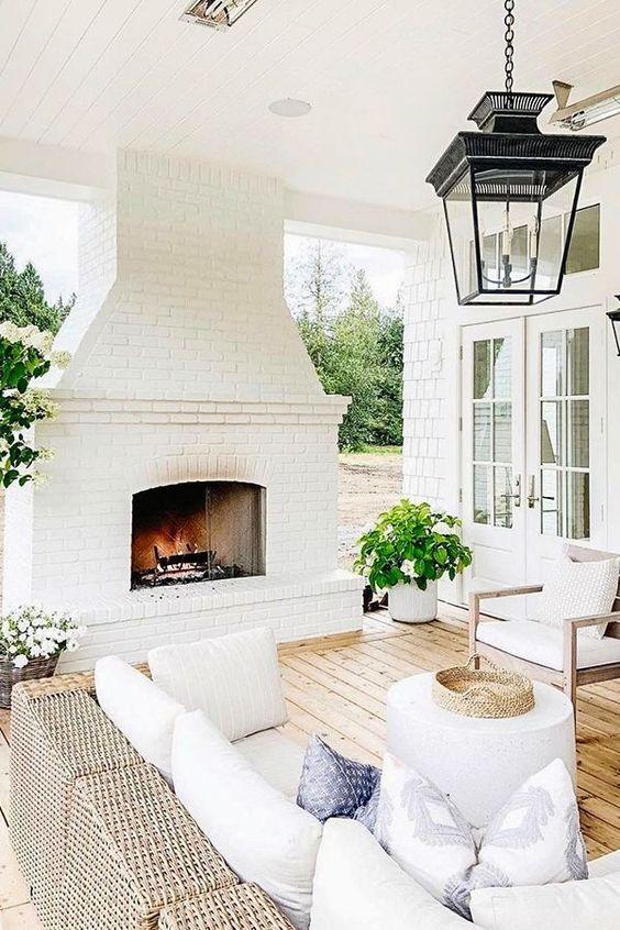 Love this beautiful covered patio with a white brick outdoor fireplace, black lantern light fixture, and seating area - patio ideas - outdoor ideas - monika hibbs