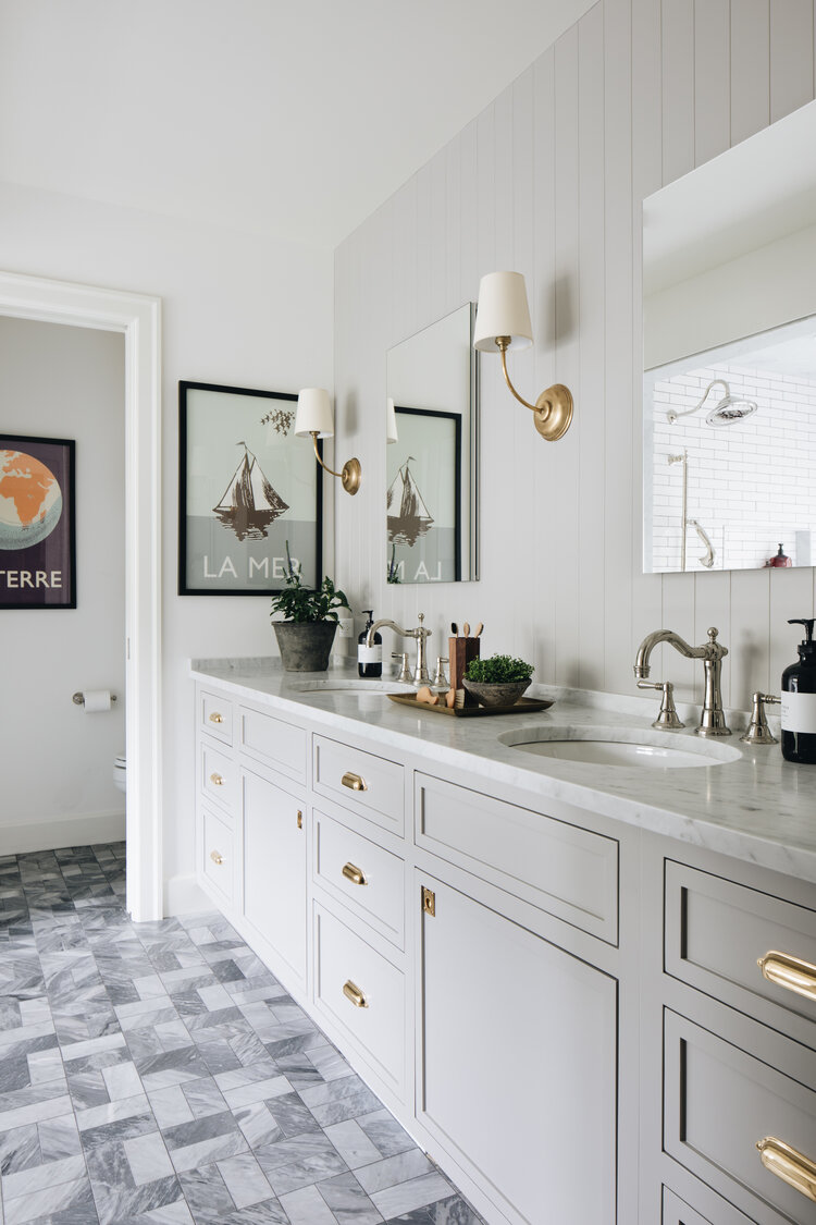Love this beautiful master bathroom with double sinks, gray vanity, brass hardware and sconces, and chrome faucets - jean stoffer interiors