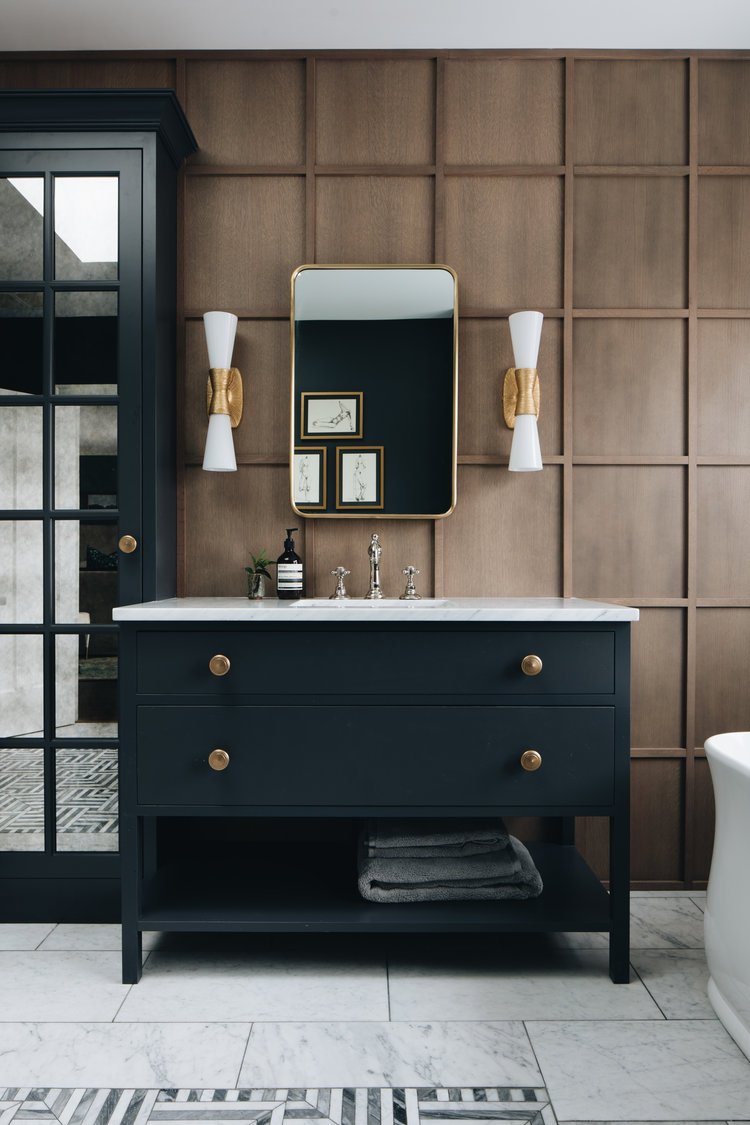 Вам понравится этот неподвластный времени дизайн ванной комнаты с темным туалетным столиком, латунными акцентами, деревянной обработкой стен и лепниной.