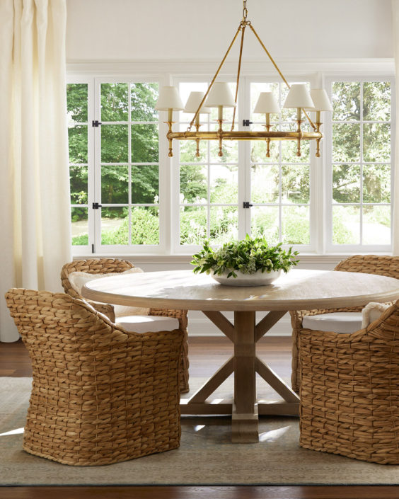 Beautiful dining room with light wood round dining table, woven dining chairs and brass chandelier with lampshades