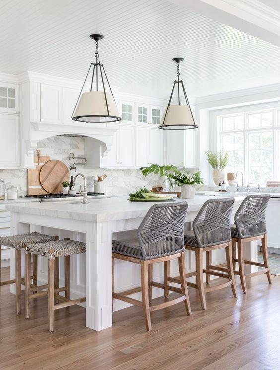 Love this beautiful kitchen design with white kitchen cabinets, a tile backsplash, black and white pendant lights, and modern woven counter stools, 