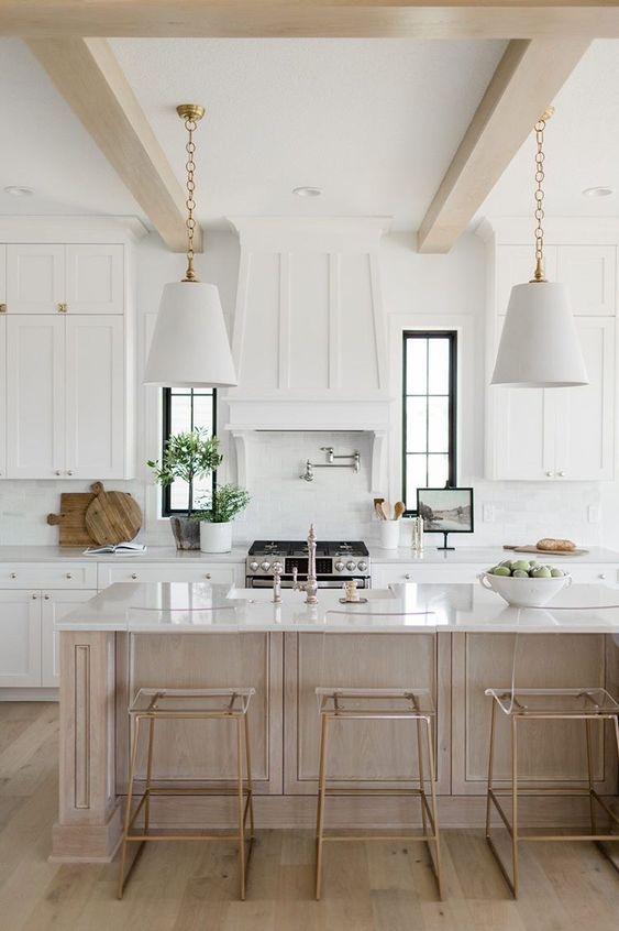 An elegant Provencal kitchen design with wood ceiling beams, white cabinets, and a whitewashed oak island.  The pendant lights over the island lend a modern touch to this beautiful space,