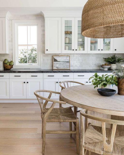 Love this beautiful kitchen dining area with a round wood dining table, woven pendant light fixture, and wishbone dining chairs - dining room ideas - dining room decor - kitchen nook - modern coastal interior design - coastal cowgirl - pure salt interiors
