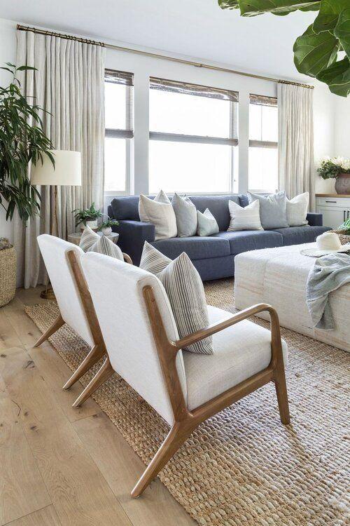 Love this beautiful living room design with two mid-century modern chairs, a denim blue sofa, jute rug, and fabric ottoman - coastal boho interiors - coastal boho living room - coastal cowgirl decor - pure salt
