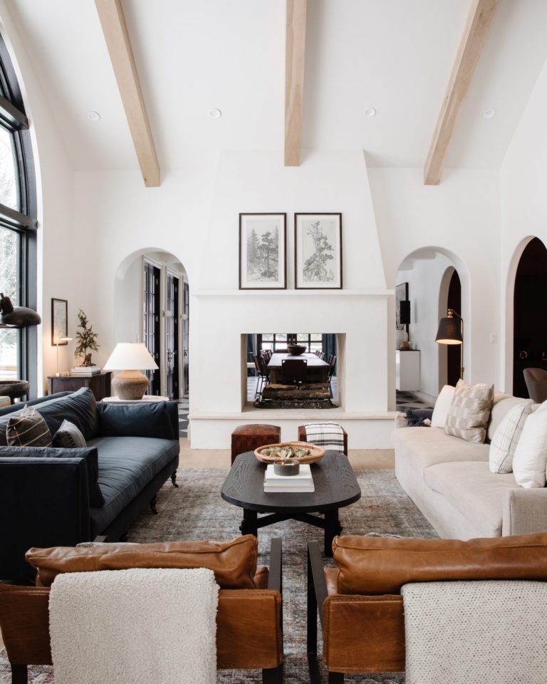 Beautiful modern living room design with white walls, wood beams, see through fireplace and arched doorway - chris loves julia - living room ideas - transitional living room