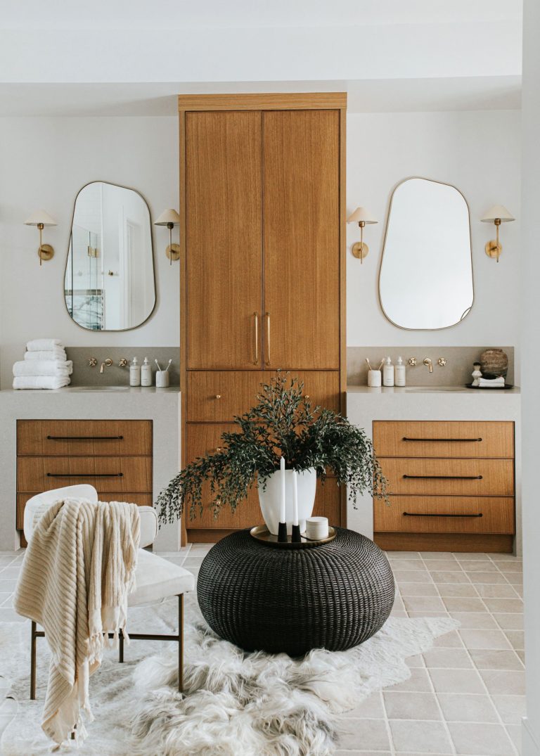 This lovely primary bathroom, from The LifeStyled Co., features polished nickel faucets, brass sconces, and a mix of brass and black cabinet pulls - modern master bathroom ideas