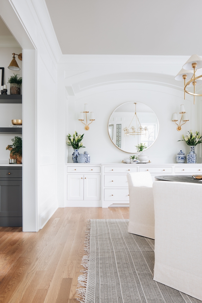 Love this beautiful transitional dining room design with white built in cabinets, a round dining table, white dining chairs and brass lighting - transitional interior design - transitional dining room - timber trails - julie howard