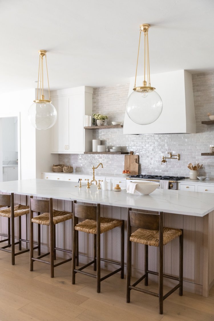 Love this beautiful modern kitchen design with a light wood island, white kitchen cabinets, woven counter stools, and oversized glass and brass globe pendant lights - ames interiors