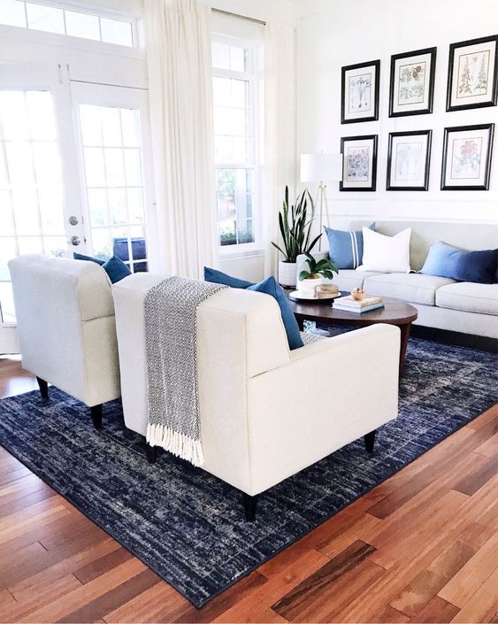 Our living room, featuring modern furniture, a dark blue rug, and a wall of botanical prints - jane at home