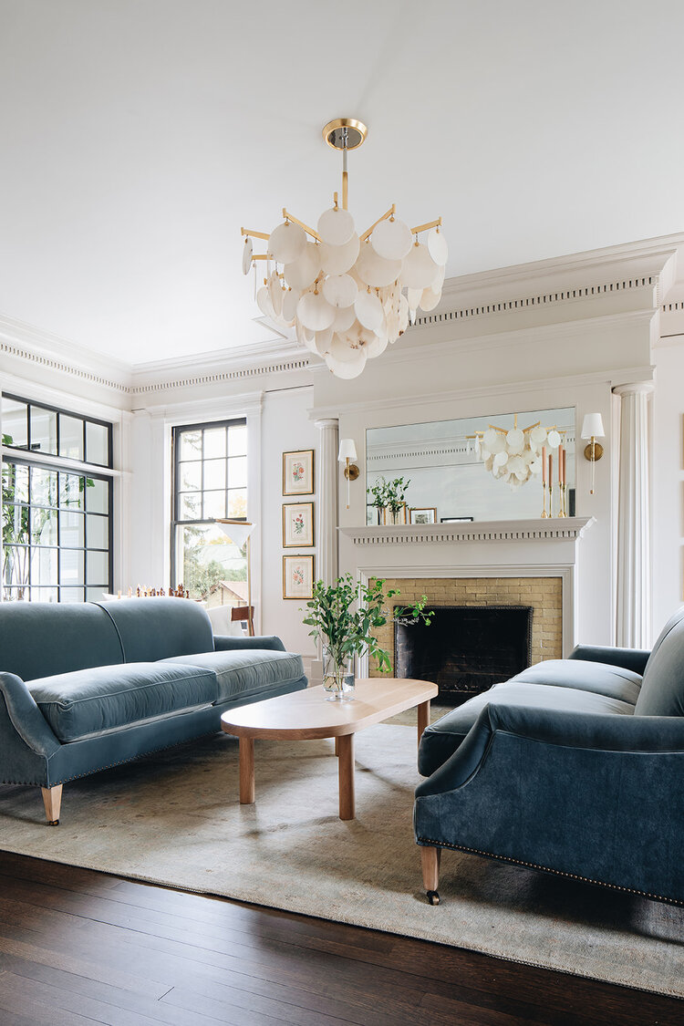Love this beautiful living room design with two blue velvet sofas, a light wood coffee table, and a capiz teardrop chandelier - living room ideas - living room decor - jean stoffer
