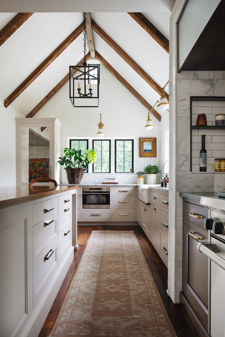 Love this beautiful kitchen design with vaulted cathedral ceilings, brass sconces, black lantern pendant, and a vintage rug - jean stoffer