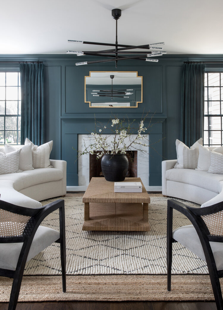 I love the two curved sofas and dark blue walls in this stylish living room.  The woven coffee table and textured rugs bring a contemporary coastal look to this space.  