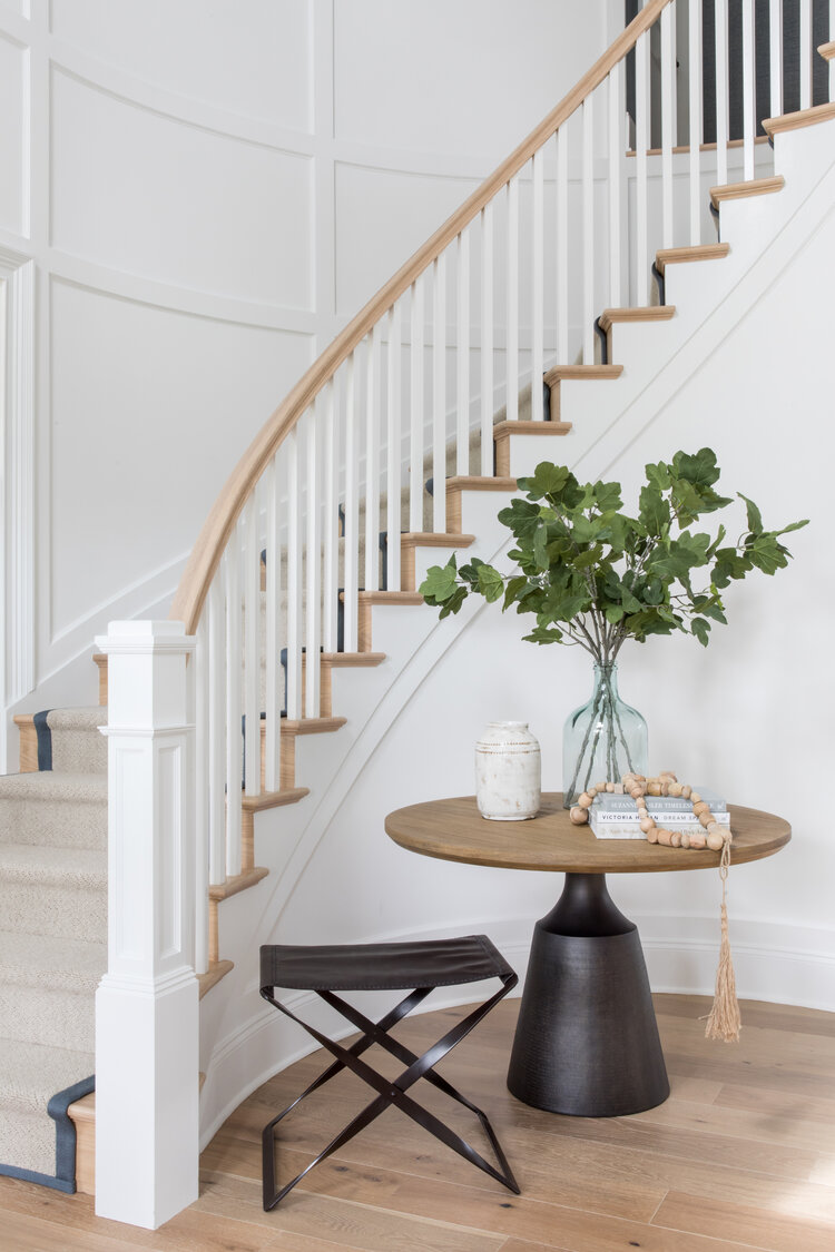 Love this beautiful entryway with a curved staircase, wall molding, and a round table and stool - entryway ideas - curves - curved stairway ideas - stairs - foyer - room ideas