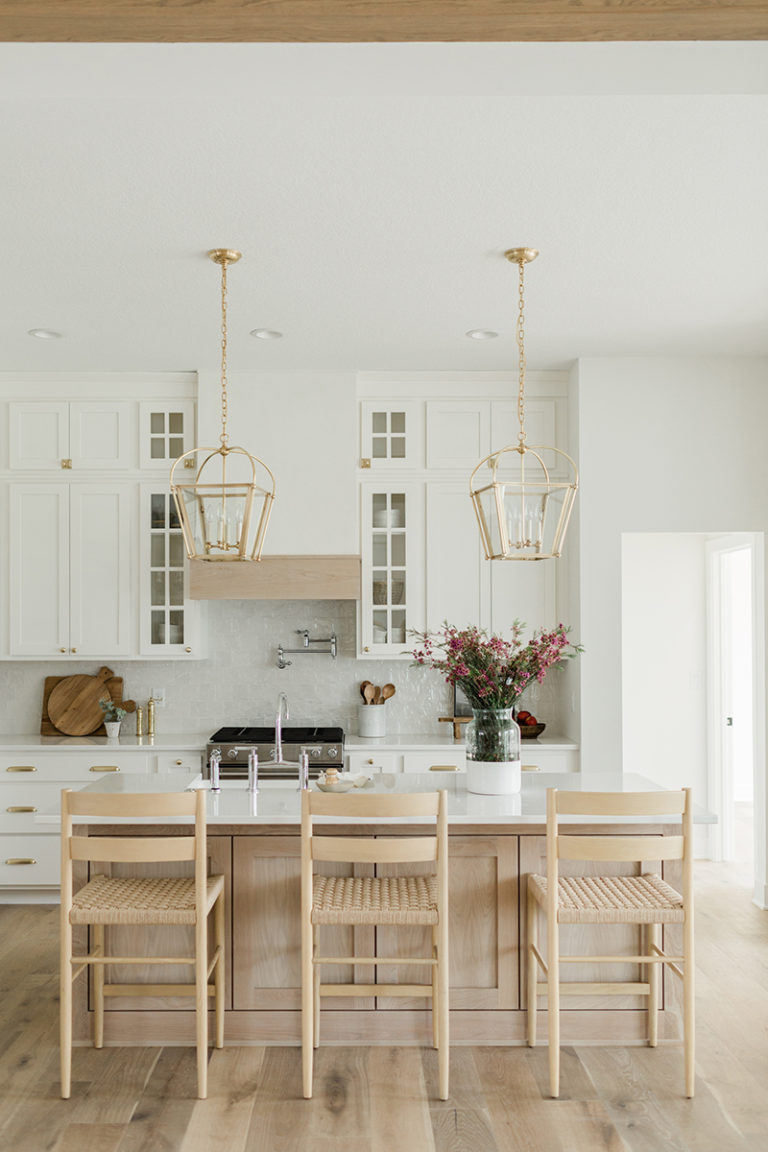 A chic and elegant kitchen design with white cabinets, a light oak island, and brass lantern style pendant lights.  