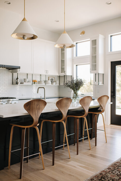 Love this beautiful modern kitchen design with elegant counter stools, a black kitchen island, white and brass cone pendant lights, and white kitchen cabinets - henri interiors