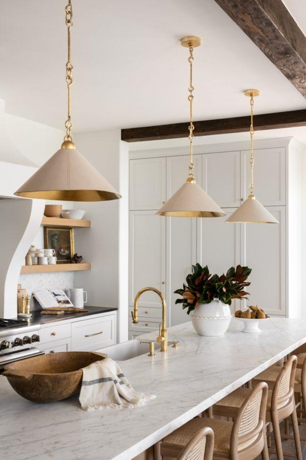 Modern kitchen with rounded cane counter stools, marble countertops on island, and modern cone pendant lights with brass faucet and hardware
