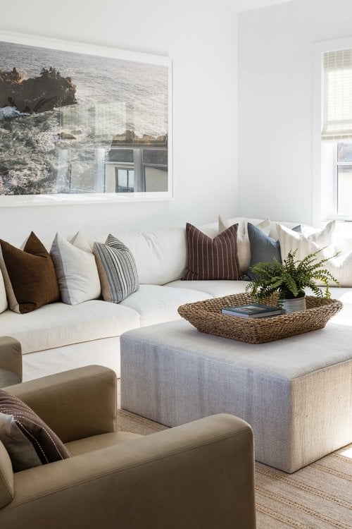 A laidback and lovely living room with oversized wall art, neutral furniture and pillows, and a large ottoman-style coffee table.  From Pure Salt Interior Design: