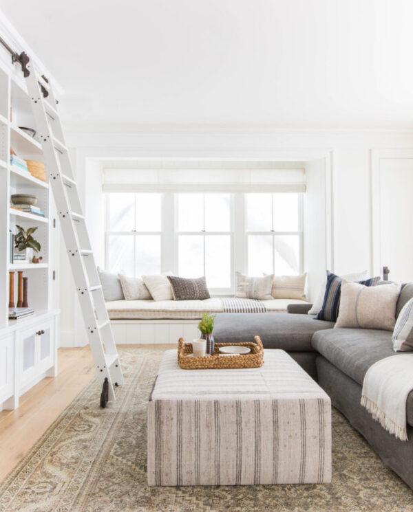 Love this beautiful modern living room and family room with a gray sectional, large ottoman, window seat, and built in shelves on the TV wall - living room ideas - living room decor - living room furniture - amber interiors - tessa neustadt