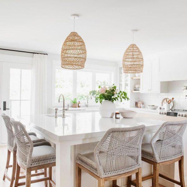 A beautiful timeless kitchen design with white cabinets, a large kitchen island, woven counter stools, and pendant lights - akb designs