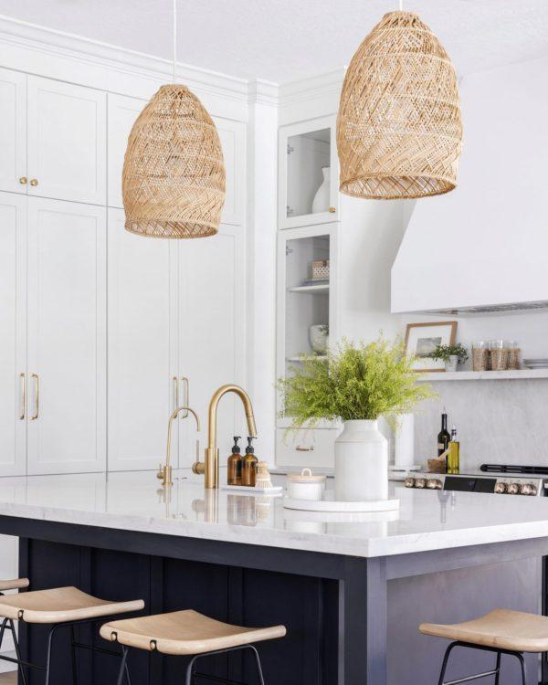A beautiful kitchen design with white cabinets, a dark kitchen island, and woven pendant lights - christina lauren