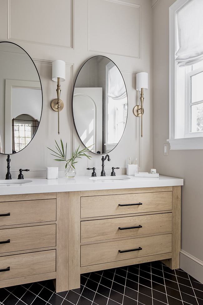 Beautiful bathroom with light wood vanity, black hardware, brass sconces and round mirrors - Jenna Sue Design