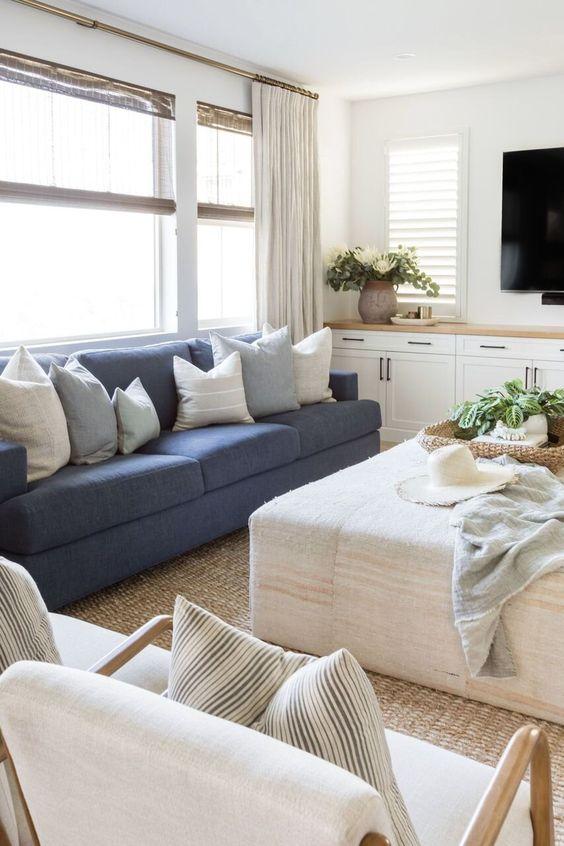 Love this beautiful living room design with a large ottoman, blue sofa, two mid-century modern chairs, jute rug, tv wall, and neutral decor and furniture - coastal cowgirl - pure salt interiors