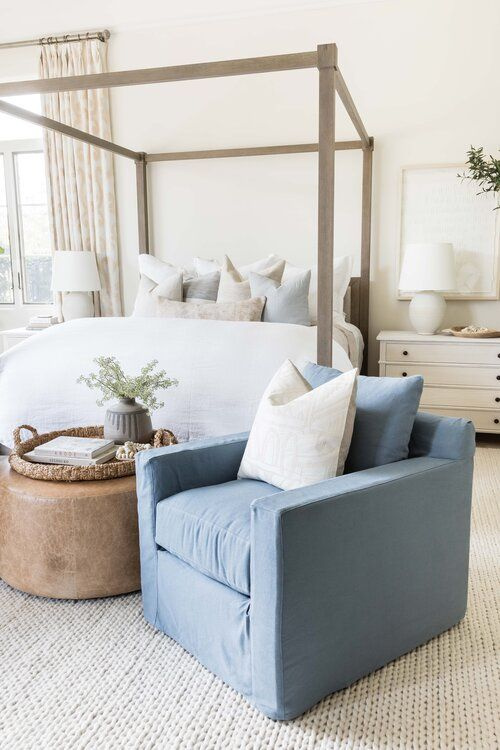 Love this beautiful bedroom design with a wood canopy bed, blue swivel chair, leather ottoman, and light neutral decor, bedding, and furniture - coastal bedroom - bedroom ideas - bedroom decor - cozy bedroom - coastal grandma - coastal cowgirl - pure salt interiors