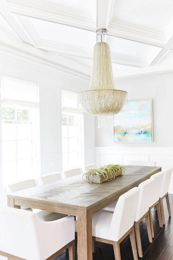 A chic modern coastal dining room with white dining chairs, a wood dining table, and beaded chandelier